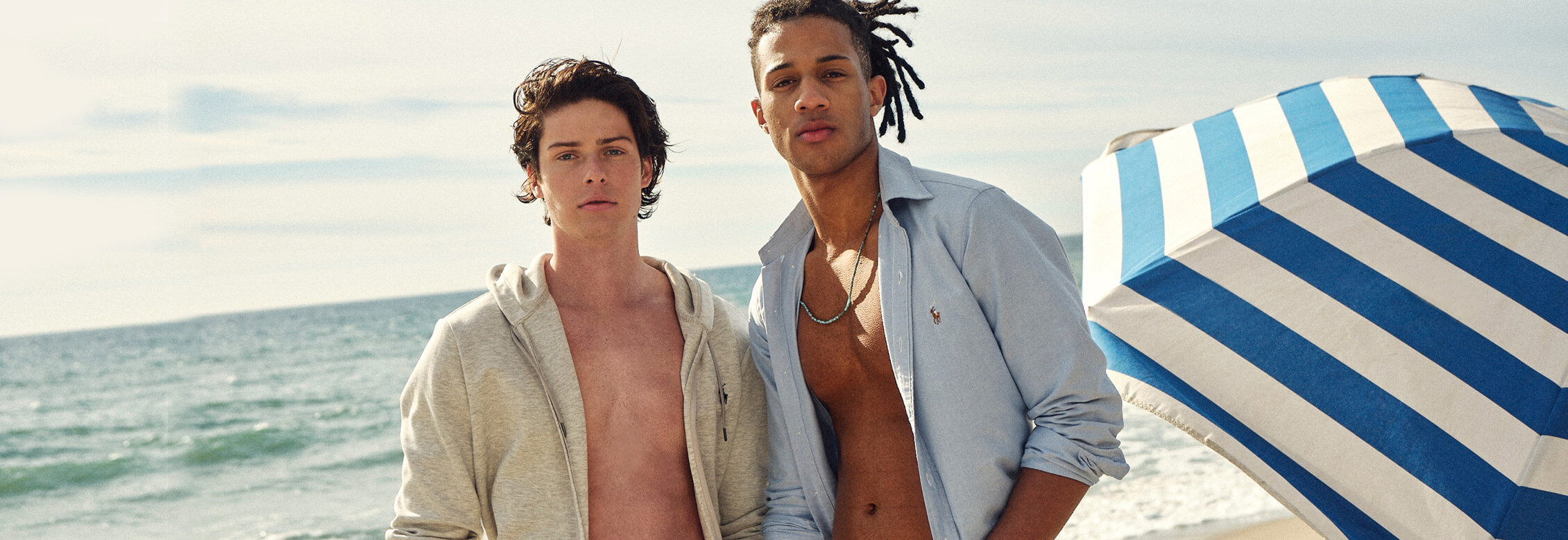 Two male models on beach with open shirts showing their abs.